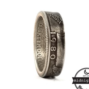 May include: Silver ring made from a 1980 quarter dollar coin. The ring is engraved with "IN GOD WE TRUST" and "QUARTER DOLLAR".