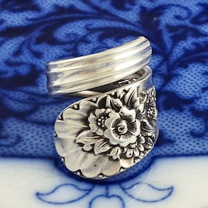 May include: A silver spoon ring with a floral design. The ring is made from a vintage spoon and is a unique piece of jewelry.