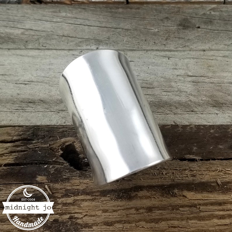 May include: A silver cuff bracelet with a smooth, polished finish. The bracelet is made of metal and has a cylindrical shape.