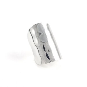 May include: A silver ring with a textured, hammered finish. The ring is wide and flat, and has a slightly curved shape.