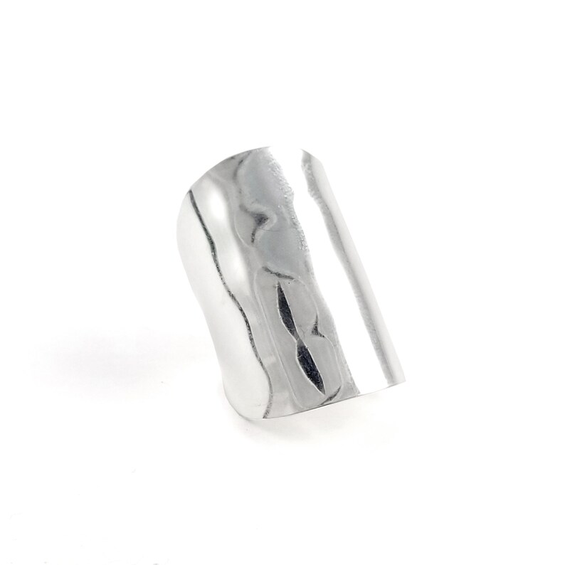 May include: A silver ring with a textured, hammered finish. The ring is wide and flat, and has a slightly curved shape.
