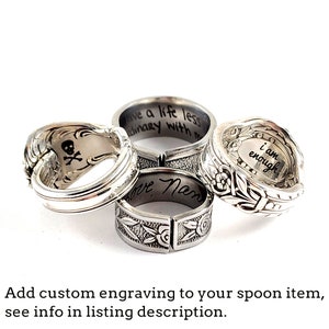 May include: Four silver spoon rings with different engraved messages. The rings are stacked on top of each other. The messages are "live a life less ordinary with me", "love Mom", "i am enough", and a skull and crossbones.