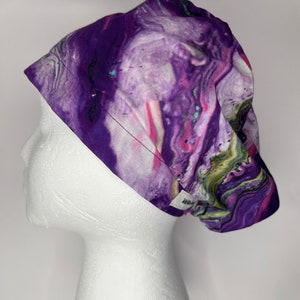 May include: Purple, pink and green abstract swirl patterned scrub hat. The hat is on a white mannequin head.