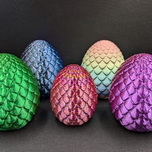 Könnte beinhalten: Fünf dracheneierförmige Ornamente mit schuppiger Textur. Die Eier sind grün, blau, rosa, hellblau und lila.