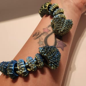 May include: A bracelet made of multiple small, textured, blue and gold-coloured pieces. The bracelet is worn on a person's wrist.