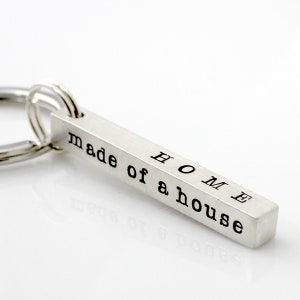 May include: Silver keychain with a bar charm that reads "HOME made of a house".