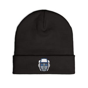 May include: A black beanie featuring an embroidered graphic on the front cuff. The embroidery depicts a stylized robot head in shades of grey, white, and blue, showcasing a geometric helmet design with blue eye-like shapes and a central face plate.