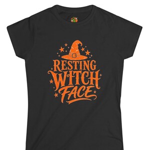 May include: A black short-sleeved t-shirt featuring an orange graphic print on the chest. The design includes a witch hat, small stars, and the text "RESTING WITCH FACE" in a stylized font. The shirt has a crew neckline and a standard fit.