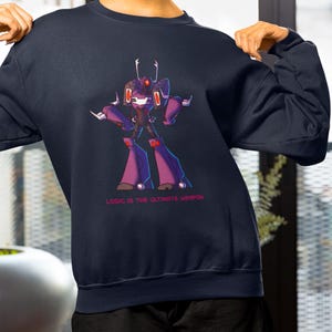 Puede incluir: Una sudadera azul marino de manga larga con un gráfico de un personaje robótico morado y negro con detalles en rojo. Debajo del personaje, el texto dice LOGIC IS THE ULTIMATE WERPON en letras rojas mayúsculas, incluyendo la ortografía.