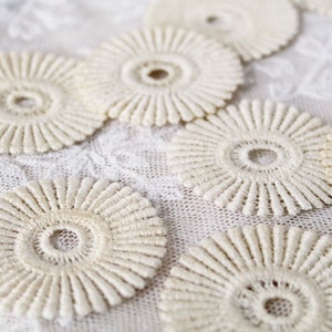 May include: A collection of off-white crocheted lace doilies with a circular design. The doilies have a raised, textured surface and a central hole.
