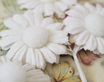 May include: White fabric flowers with a fuzzy center, arranged on a background with a butterfly pattern.
