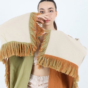 Könnte beinhalten: Ein mehrfarbiger, gefranste Kimono in einem Farbschema aus Hellgrün, Beige und Rostorange. Der Kimono hat eine lockere Passform und ist aus einem leichten Stoff gefertigt.