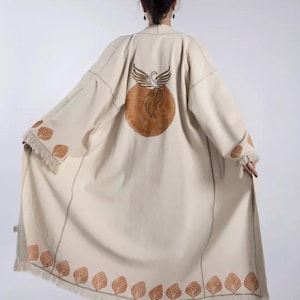 May include: Cream-colored long coat with a phoenix design on the back. The coat features leaf patterns in brown along the sleeves and hem. The coat has a fringed edge and a loose, flowing design.