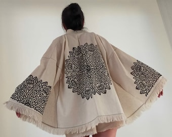 May include: A cream-colored kimono with black floral embroidery. The kimono has a fringed hem and is made of a lightweight fabric.
