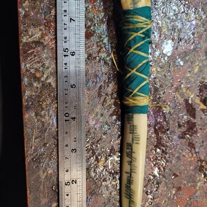 May include: A handcrafted ivory-colored dagger with a black stone at the top. The handle is wrapped in teal fabric and tan twine. The blade features etched markings. A metal ruler shows the dagger is approximately 7 inches long.
