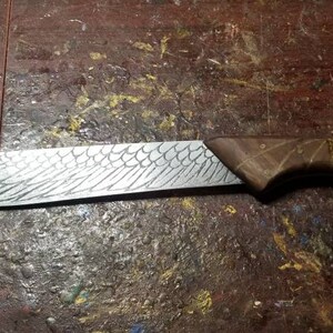 May include: A handcrafted knife with a wooden handle and a blade etched with a wing design. The blade is approximately 10 inches long, and the handle is a dark brown color. The knife is designed for cutting and slicing.