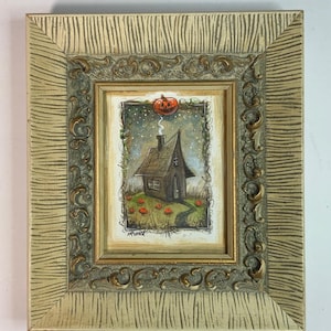May include: A framed Halloween-themed artwork. The painting shows a small, dark house with a tall, pointed roof, a smoking chimney, and a floating pumpkin. The frame is ornate, with a textured, light-coloured finish and decorative gold accents.
