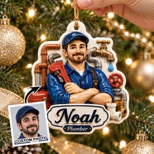 May include: A custom Christmas ornament featuring a sculpted plumber with a beard and blue cap, holding a red pipe wrench. The ornament includes copper and silver pipes, a faucet, and a red valve. A nameplate displays the text Noah and Plumber.