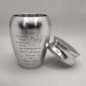 May include: A brushed silver urn with a removable lid. The urn has engraved text that reads "Sister" and a message about a bond between sisters. The urn is designed to hold ashes and has space for a name and dates.