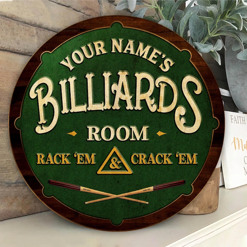 May include: Round wooden sign with a green center and a dark brown border. The sign reads "YOUR NAME'S BILLIARDS ROOM" in cream-colored lettering. Below, it says "RACK 'EM & CRACK 'EM". Two crossed pool cues are at the bottom.