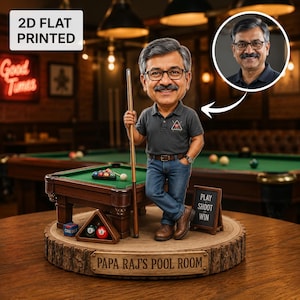 May include: A custom bobblehead figurine of a man with glasses and a mustache, wearing a gray polo shirt and blue jeans, holding a pool cue. The figure stands on a wooden base labeled "PAPA RAJ'S POOL ROOM" next to a miniature pool table, balls, and a sign reading "PLAY SHOOT WIN."