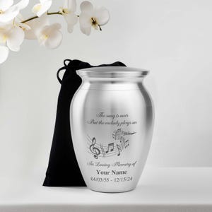 May include: Silver cremation urn with a musical note design and the inscription "The song is over, But the melody plays on". The urn also includes the text "In Loving Memory of" followed by a space for a name and dates.