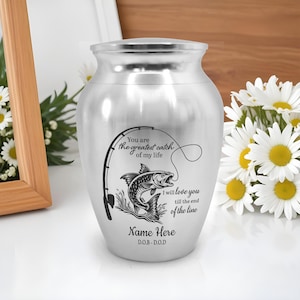 May include: A silver urn with a fishing-themed design. The urn features a fishing rod, a fish, and the text "You are the greatest catch of my life." It also includes the text "I will love you till the end of the line" and space for a name and dates.