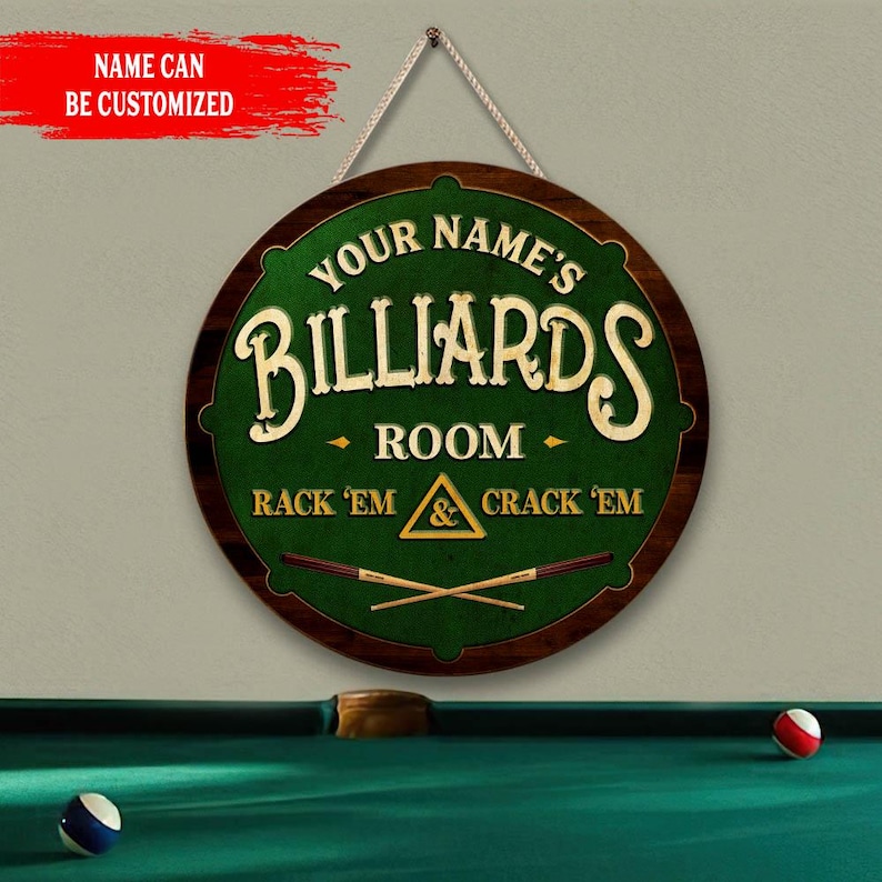 May include: A round wooden sign for a billiards room, featuring the text "YOUR NAME'S BILLIARDS ROOM" in a stylized font. The sign has a green center with the words "RACK 'EM & CRACK 'EM" and crossed pool cues. A string is attached for hanging.