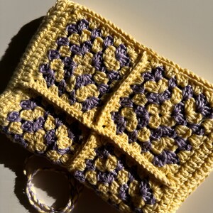 May include: A crocheted pouch with a yellow and purple granny square pattern. The pouch has a drawstring closure.