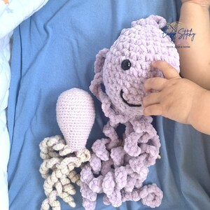 Puede incluir: Dos peluches de pulpo de crochet. Uno es de color morado claro con una cara sonriente y ojos negros. El otro es de color beige claro con una cabeza redonda y tentáculos rizados.