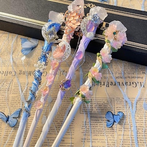 May include: Four decorative wands with crystal and floral details. Each wand has a unique colour scheme, including blue, pink, and purple, with intricate features like moons, butterflies, and gemstones. The wands are presented on a vintage newspaper background.