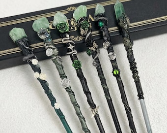 May include: A collection of seven handcrafted wands, each with unique designs. The wands feature green crystal tips, intricate detailing with snakes, roses, and other embellishments. The wands are in various colors, including black, green, and silver.