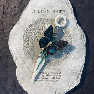 May include: A white stone with a green and black butterfly charm attached to a white metal rod. The stone has the words "Tree of Life" and "Wisdom" inscribed on it. The charm is a representation of the journey through life and the universe, spirit, earth, and the cosmos.