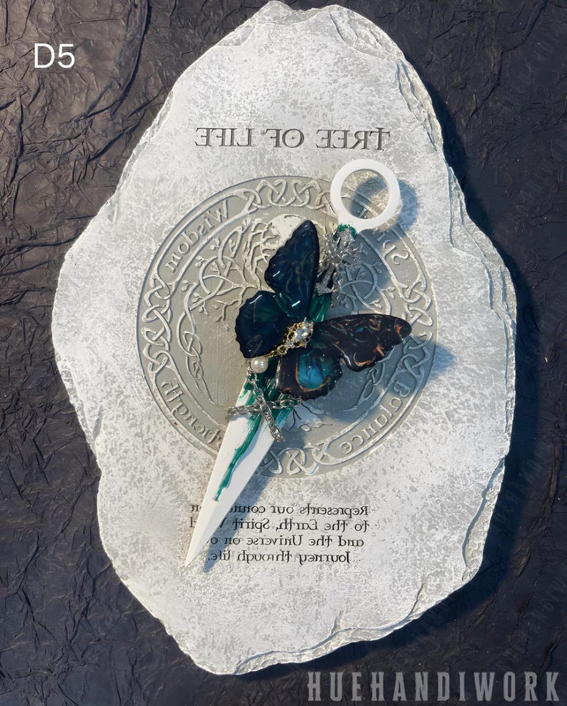 May include: A white stone with a green and black butterfly charm attached to a white metal rod. The stone has the words "Tree of Life" and "Wisdom" inscribed on it. The charm is a representation of the journey through life and the universe, spirit, earth, and the cosmos.