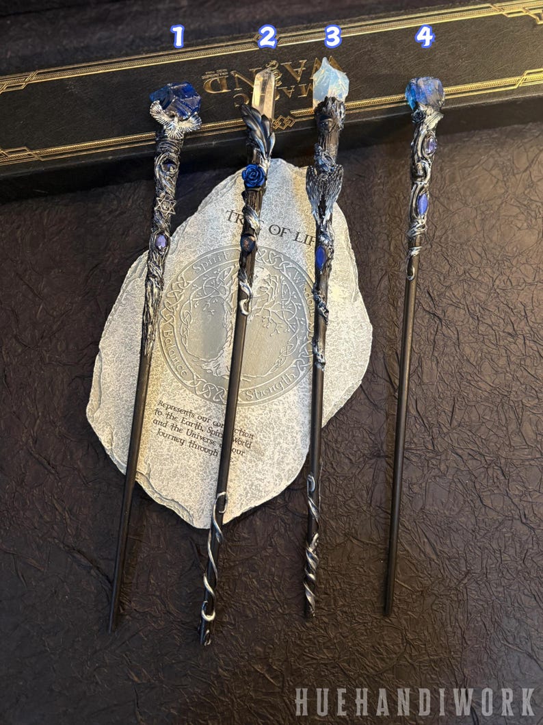 Puede incluir: Cuatro varitas de fantas&iacute;a con dise&ntilde;os intrincados. Cada varita presenta un mango oscuro y una parte superior decorativa con detalles azules o transparentes en forma de cristal. Las varitas se exhiben sobre una superficie similar a una piedra con el texto "TREE OF LIFE" y "HUEHANDIWORK".