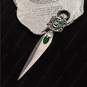 May include: A silver and green snake charm with a green gem stone. The charm is attached to a black leather cord. The charm is on a gray stone background with the words "All throughout the universe on every spirit, earth, and connection, not just you, yourself's experience".