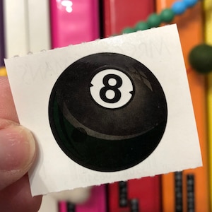 May include: A black and white 8-ball sticker with a glossy finish.