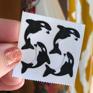 May include: A sheet of four black and white orca stickers. The orcas are in a jumping pose with their tails in the air.