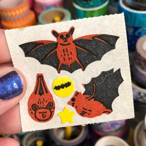 May include: A sheet of Halloween-themed stickers featuring a red bat, a black bat, a yellow bat, a yellow star, and a red pumpkin with a cute face.