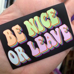 May include: A black sticker with the text "BE NICE OR LEAVE" in rainbow-colored letters. The letters are in a retro, 3D style.
