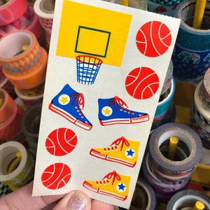 May include: A sheet of stickers featuring basketball-themed designs. The stickers include a basketball hoop, basketballs, and sneakers in blue, yellow, and red.