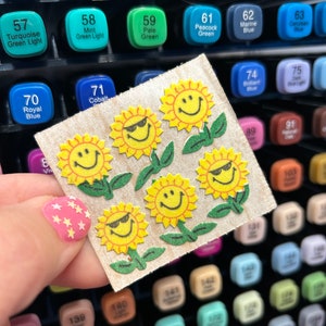 May include: A sheet of stickers with five smiling yellow sunflowers. The sunflowers have green stems and leaves. The stickers are on a brown background.