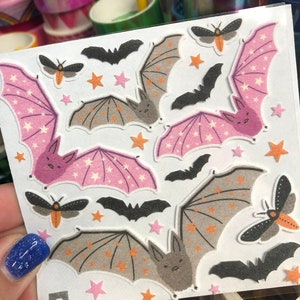 May include: A sheet of stickers featuring bats and moths with a glittery, textured finish. The bats are in shades of gray and pink with white stars. The moths are orange and black. The sheet has the text "www.pipsticks.com" printed on it.