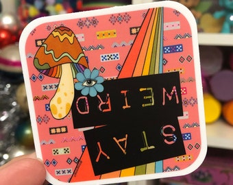May include: A pink and black sticker with a rainbow, a mushroom, and the text "STAY WEIRD".