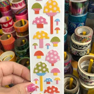 May include: A sheet of colorful mushroom stickers with white polka dots. The stickers are on a white background and have a variety of colors, including pink, yellow, green, blue, and orange.