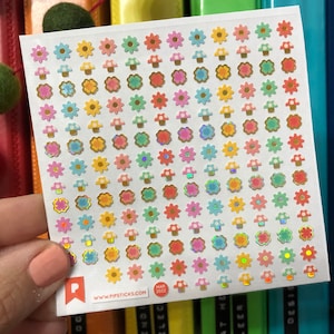 May include: A sheet of colorful flower and mushroom stickers with a holographic finish. The stickers are arranged in rows on a white background. The sheet has a website address and a date printed on it.