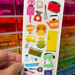 May include: A sheet of vintage kitchen-themed stickers featuring a pink cat clock, a red toaster, a yellow refrigerator, a green stand mixer, a brown owl, and a blue and white mixing bowl. The stickers are on a white background and have a vintage color scheme.
