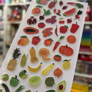 May include: A sheet of colorful fruit and vegetable stickers. The stickers include illustrations of a pineapple, watermelon, apple, orange, banana, and more. The stickers are on a clear backing.