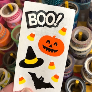 May include: A sheet of Halloween stickers with a black bat, a witch's hat, a pumpkin, candy corn, and the word "BOO!" in black letters.