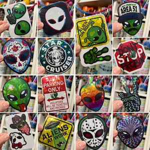 May include: A collection of 12 holographic stickers featuring various alien designs. The stickers include a skull with flowers, a spaceship, a stop sign, a peace sign, and an alien with a tongue sticking out. The stickers are all on a white background.